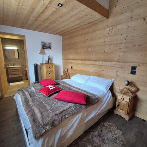 A bedroom with a wooden ceiling, a bed with a fluffy blanket and red pillows, a wooden nightstand, a mirror, and a small wooden cabinet. - Luxury apartment near downtown and the recreation center (Samoëns)