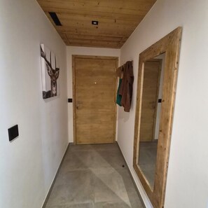 Un couloir avec une porte en bois, un porte-manteau sur lequel sont suspendus des vêtements et un tableau encadré au mur.