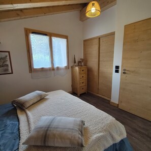 Une chambre à coucher comprenant un lit, une commode, une armoire, une fenêtre avec des rideaux et un luminaire suspendu.