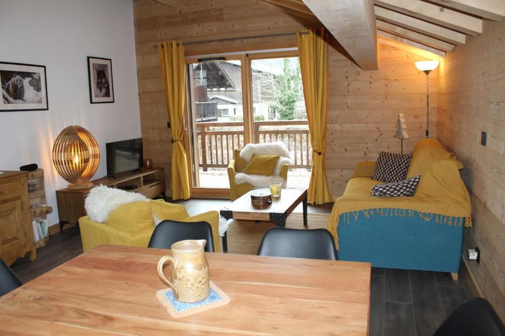 A cozy room with a wooden interior, a dining table with chairs, a sofa, and a television.