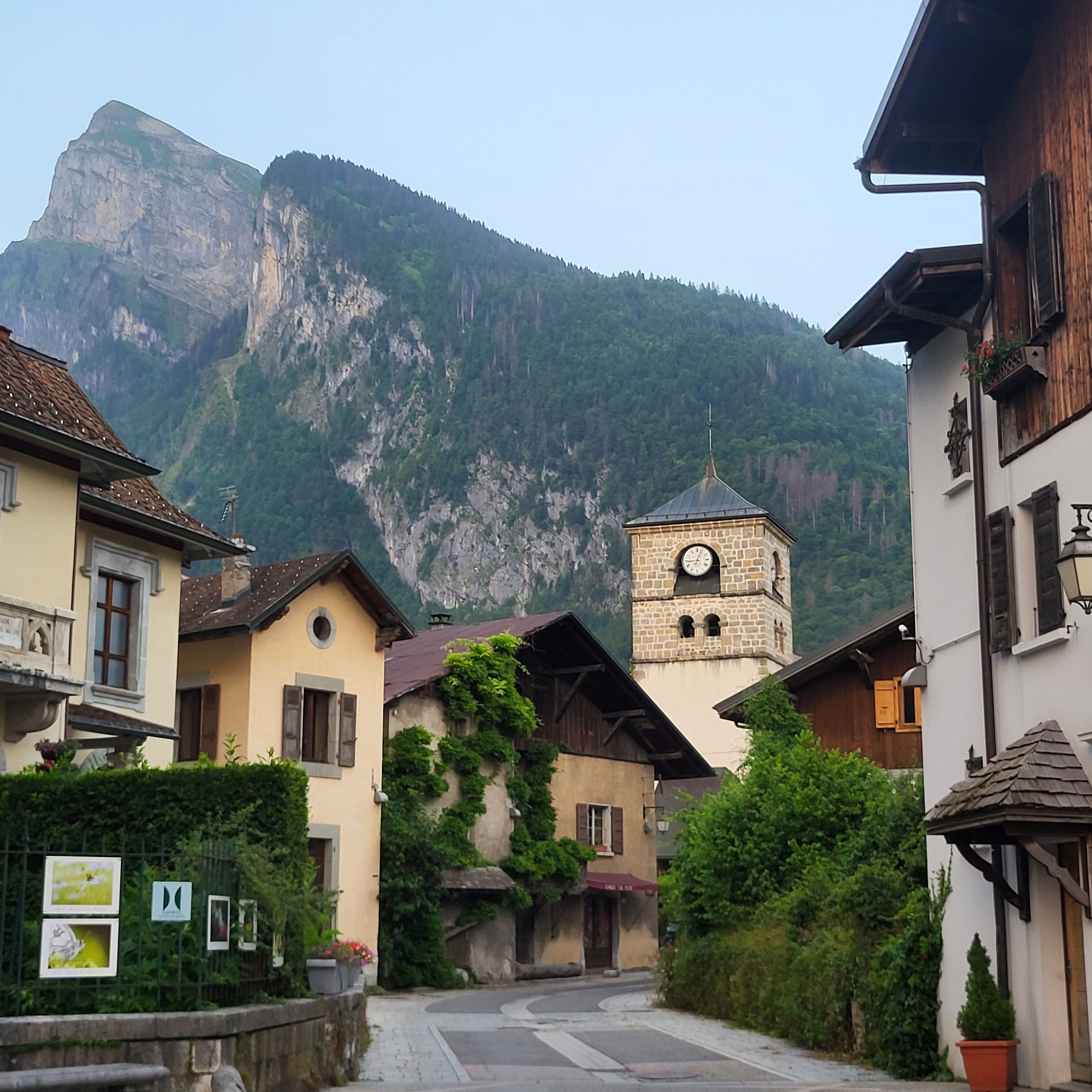 Ein Bergdorf mit traditioneller Architektur, einem markanten Glockenturm und einer steilen Bergkulisse.