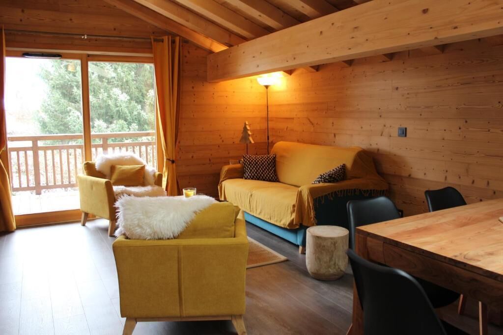 Interior de una cabaña de madera con sofá, sillas, una mesa y una lámpara.