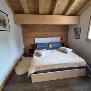 Ein Schlafzimmer mit Holzbalkendecke, einem Bett mit flauschiger weißer Bettdecke und einem kleinen Nachttisch mit Lampe.