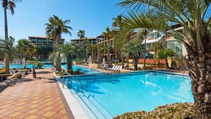 A resort pool area with multiple swimming pools, palm trees, and lounge chairs. - Red Rooster (Panama City Beach)