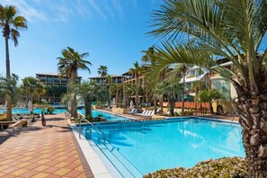 Ein Resort-Poolbereich mit mehreren Schwimmbecken, Palmen und Liegestühlen.
