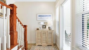 A hallway with a wooden staircase, a light-colored console table with decorative items, and a patterned rug. - Red Rooster (Panama City Beach)