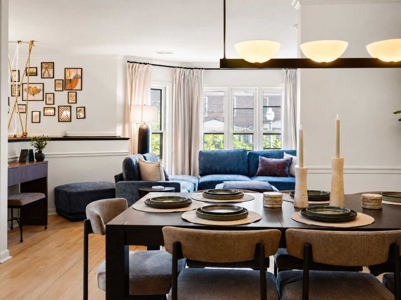 Un comedor con una mesa dispuesta para cuatro personas, un sofá azul al fondo y una pared decorada con cuadros.