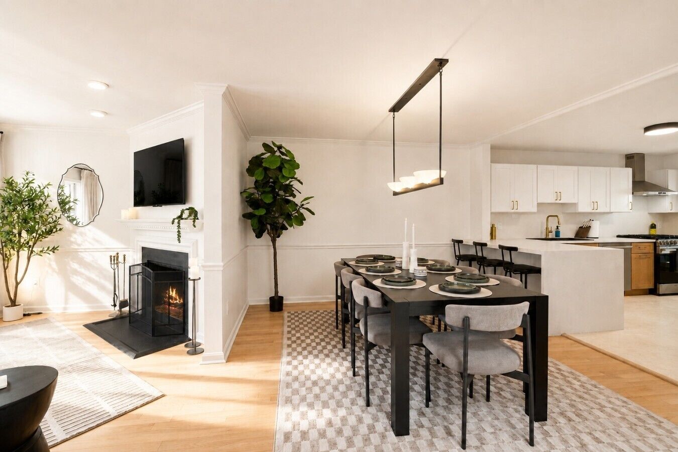 Een moderne woonkamer met een open haard, een eethoek met een geruit kleed, en een keuken met witte kasten.