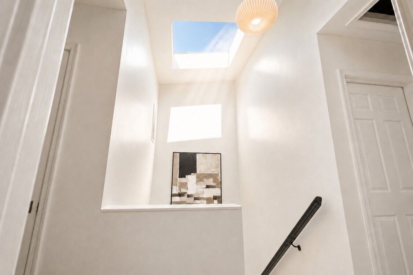 Una escalera estrecha con tragaluces y un ventanal pequeño, que conduce a una habitación con una puerta blanca.