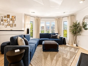 A living room with a sectional sofa, a coffee table, and a large window with curtains. - The Monroe by Willow · Mt Pleasant · 4BR Residence (Washington)