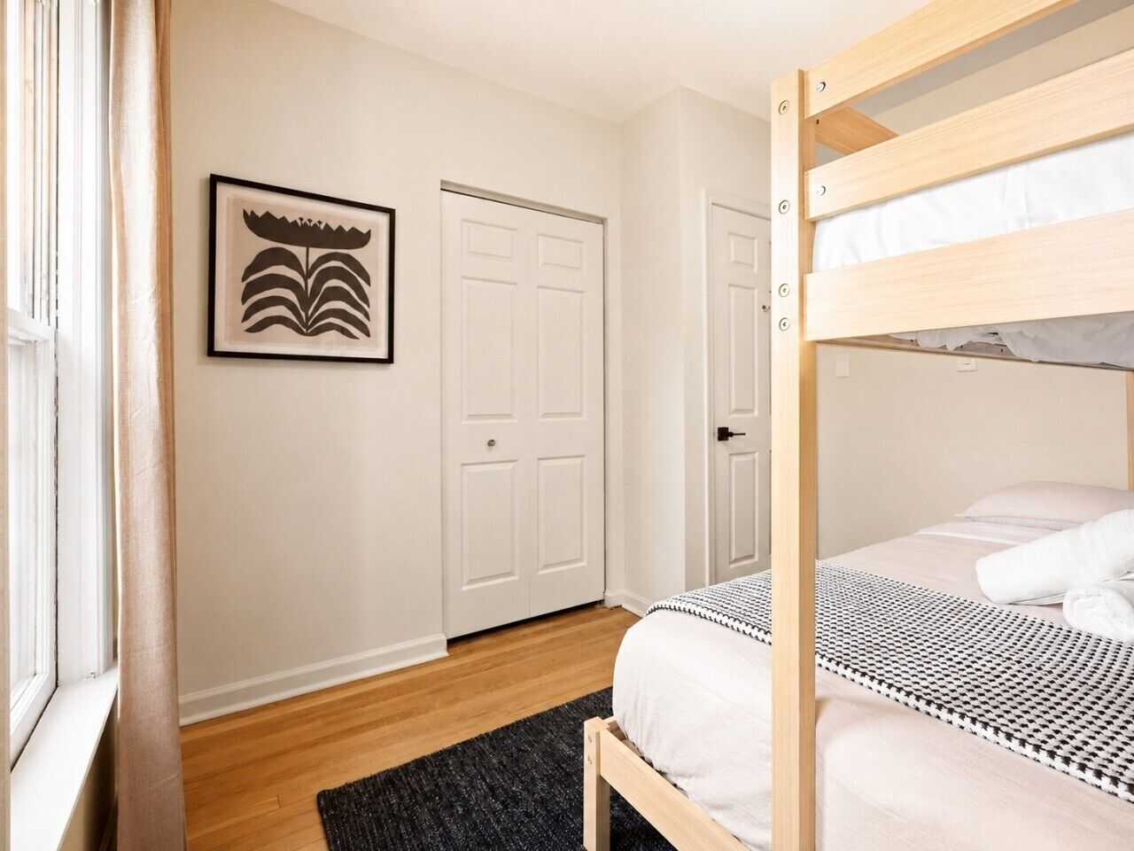 Une chambre avec un lit superposé, une porte, un tableau encadré au mur et une fenêtre.