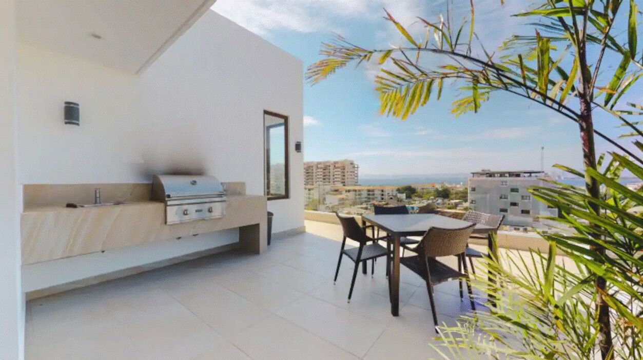 A modern kitchen with a built-in grill, a dining area with a table and chairs, and a view of the cityscape.
