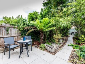 Un patio con mesa y sillas, rodeado de abundante vegetación y una valla de madera.