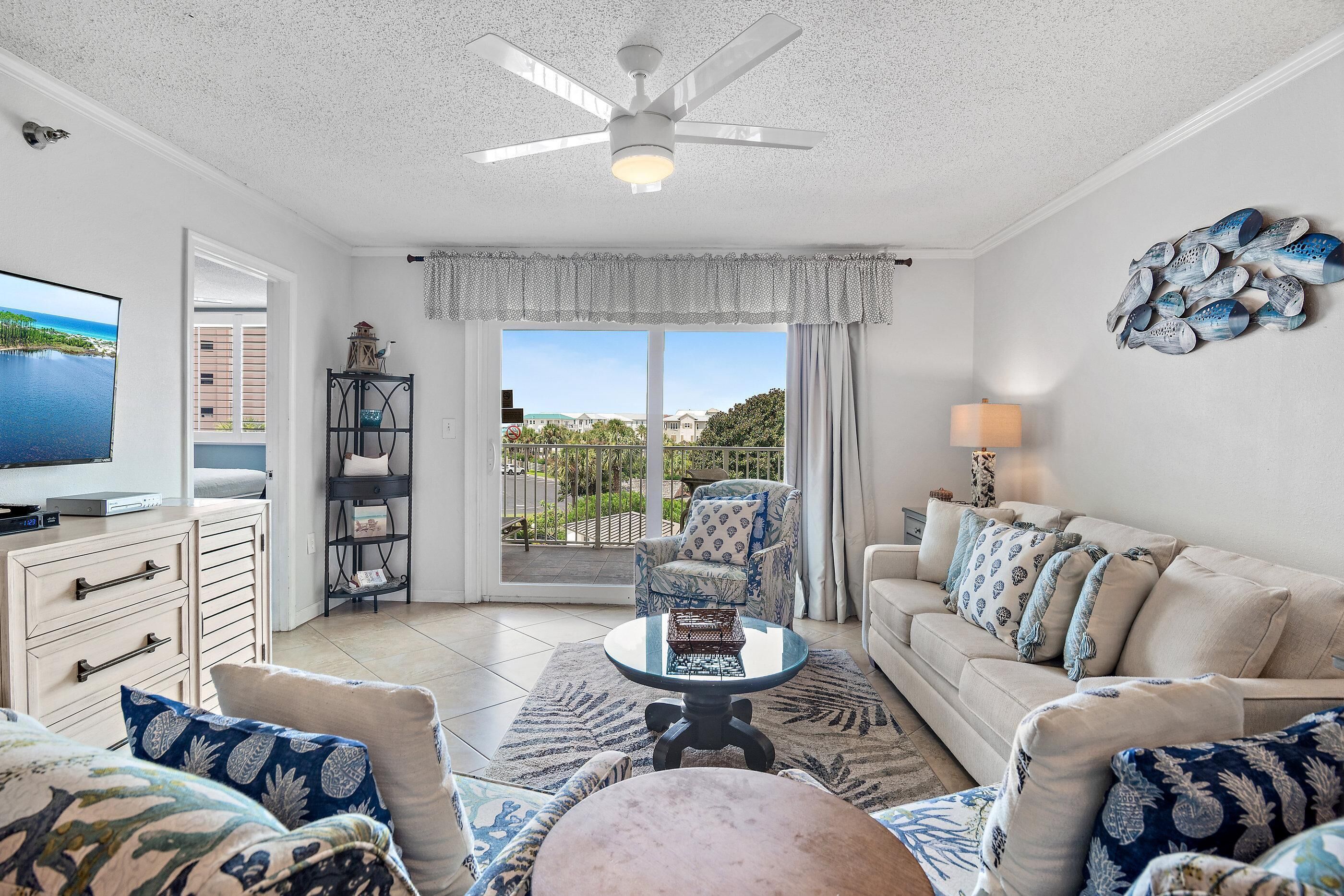 A living room with a television, a ceiling fan, a sofa, and a view of the outdoors.