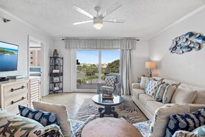 A living room with a television, a ceiling fan, a sofa, and a view of the outdoors. - The Islander 314 Dolphin Cove (Destin)