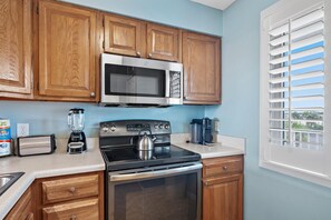 A kitchen with wooden cabinets, a stainless steel microwave, a toaster, a kettle, and a coffee maker. - The Islander 314 Dolphin Cove (Destin)