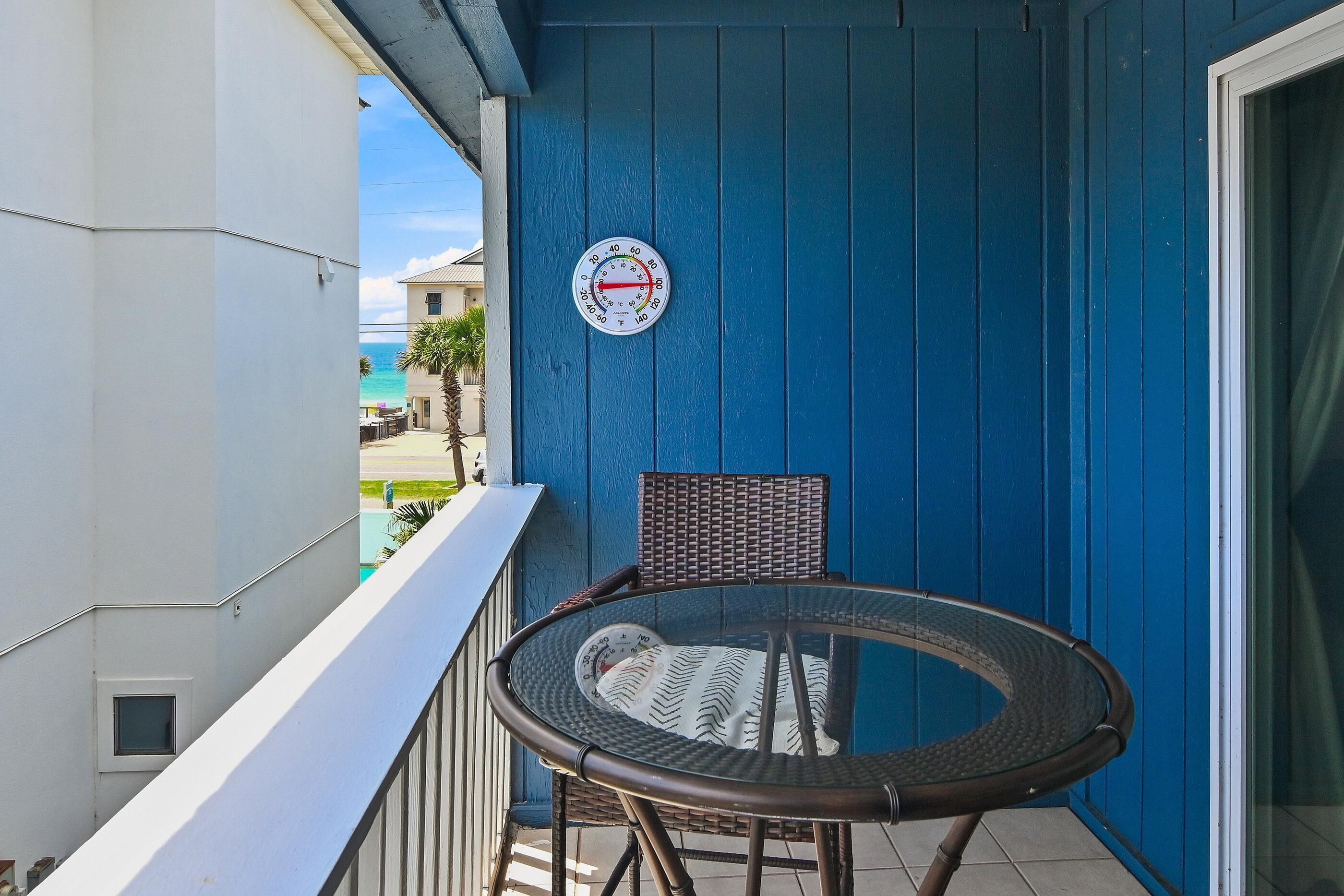 Ein Balkon mit einem runden Tisch, einem Stuhl, einem Thermometer und Blick auf den Ozean.