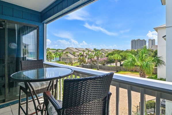 A balcony with a glass table and wicker chairs, overlooking a residential area with houses and palm trees. - Lakeview #9 - Paradise By The Gulf (Miramar Beach)