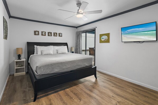 Een slaapkamer met een bed, nachtkastje, plafondventilator, raam met uitzicht en wanddecoraties.