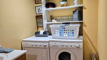 A laundry room with a washing machine, dryer, and shelves above containing laundry supplies.