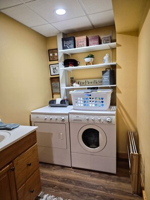 A laundry room with a washing machine, dryer, and shelves above containing laundry supplies.