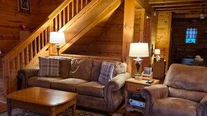 A cozy log cabin interior with a wooden staircase, a sofa set, a coffee table, and a rug.