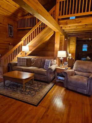 A cozy log cabin interior with a wooden staircase, a sofa set, a coffee table, and a rug.