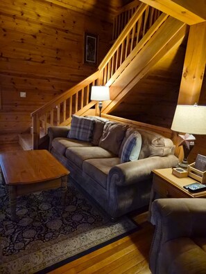 Ein gemütliches Wohnzimmer mit einer Holztreppe, einem Sofa, einem Couchtisch und einer Lampe.