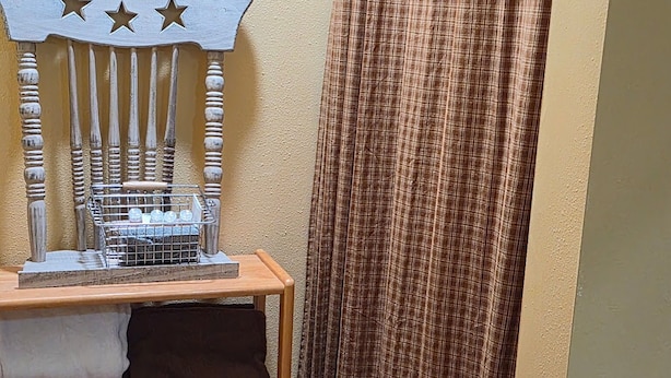A corner of a room with a wooden bench, a metal rack with bottles, and a curtain.