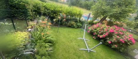 A well-maintained garden with a variety of plants and flowers, a lawn, and a metal structure in the center.