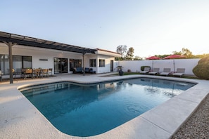 Ein Pool mit einer Terrassenfläche, einem Grill und Liegestühlen.