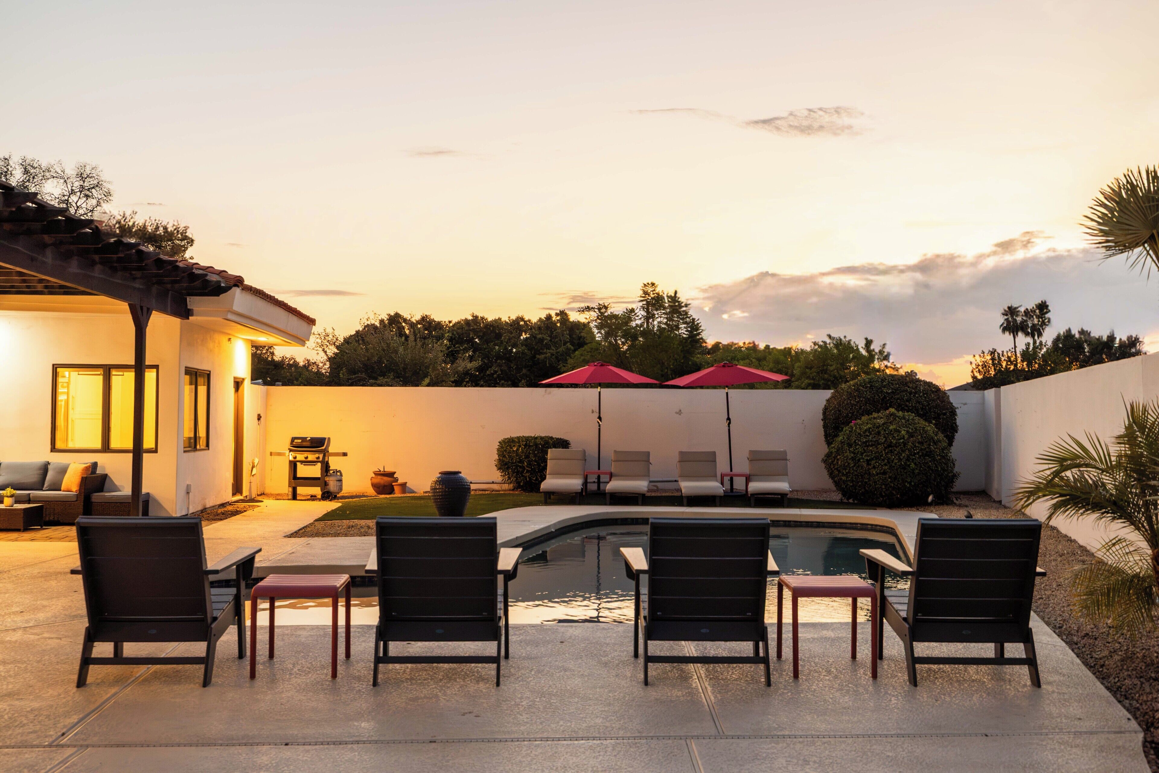 Un espace piscine avec des chaises longues et des parasols, un barbecue et une maison dotée d’une terrasse.