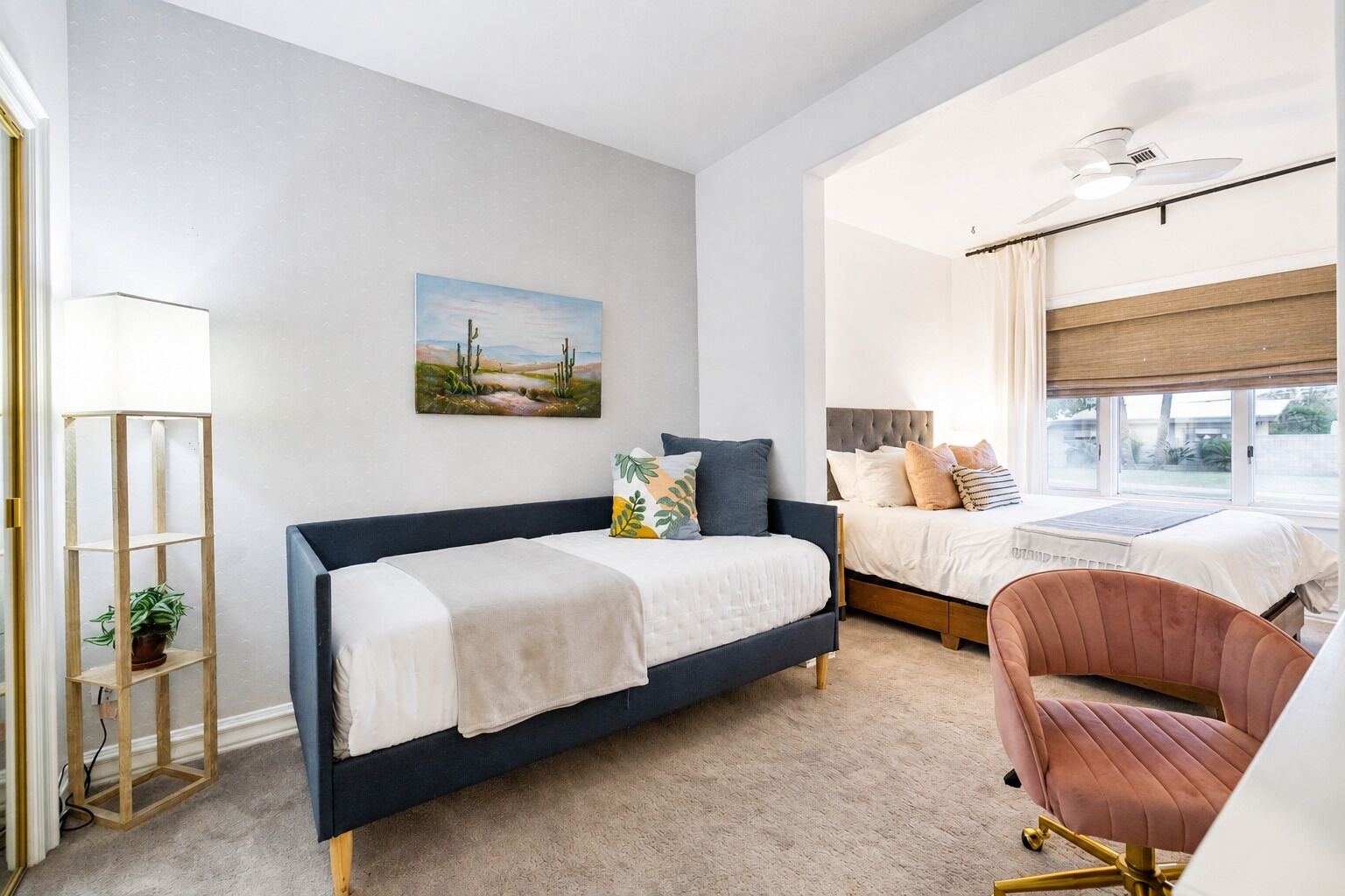 A bedroom with a bed, a desk, a chair, a plant, and a painting on the wall.