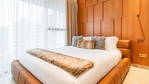 Une chambre d’hôtel moderne avec un grand lit, une tête de lit en bois et une vue sur la ville grâce à de grandes fenêtres.