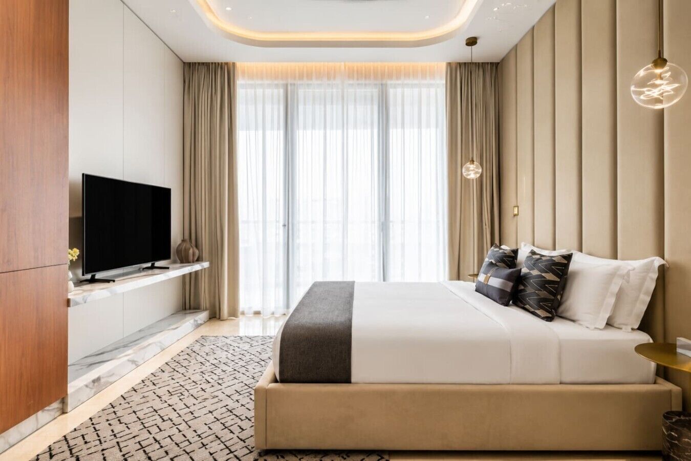 A modern hotel room with a large bed, a flat-screen TV, and a view of the city through large windows.