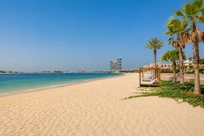 A beach with a clear sky, a sandy shore, and a wooden structure with a bed. - Ellington Beach House (Dubai)
