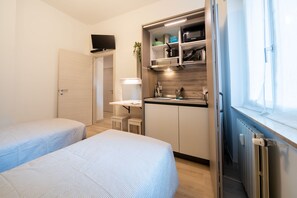 Een kleine kamer met twee bedden, een kitchenette en een raam.