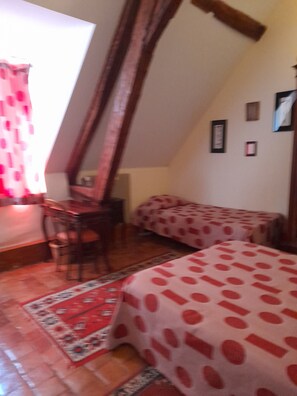 A room with a sloped ceiling, a dining table, two beds with polka dot bedding, and a red patterned rug.