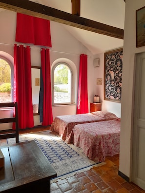 Una stanza con due letti, un tavolo di legno, un tappeto decorato e un'ampia finestra con tende rosse.