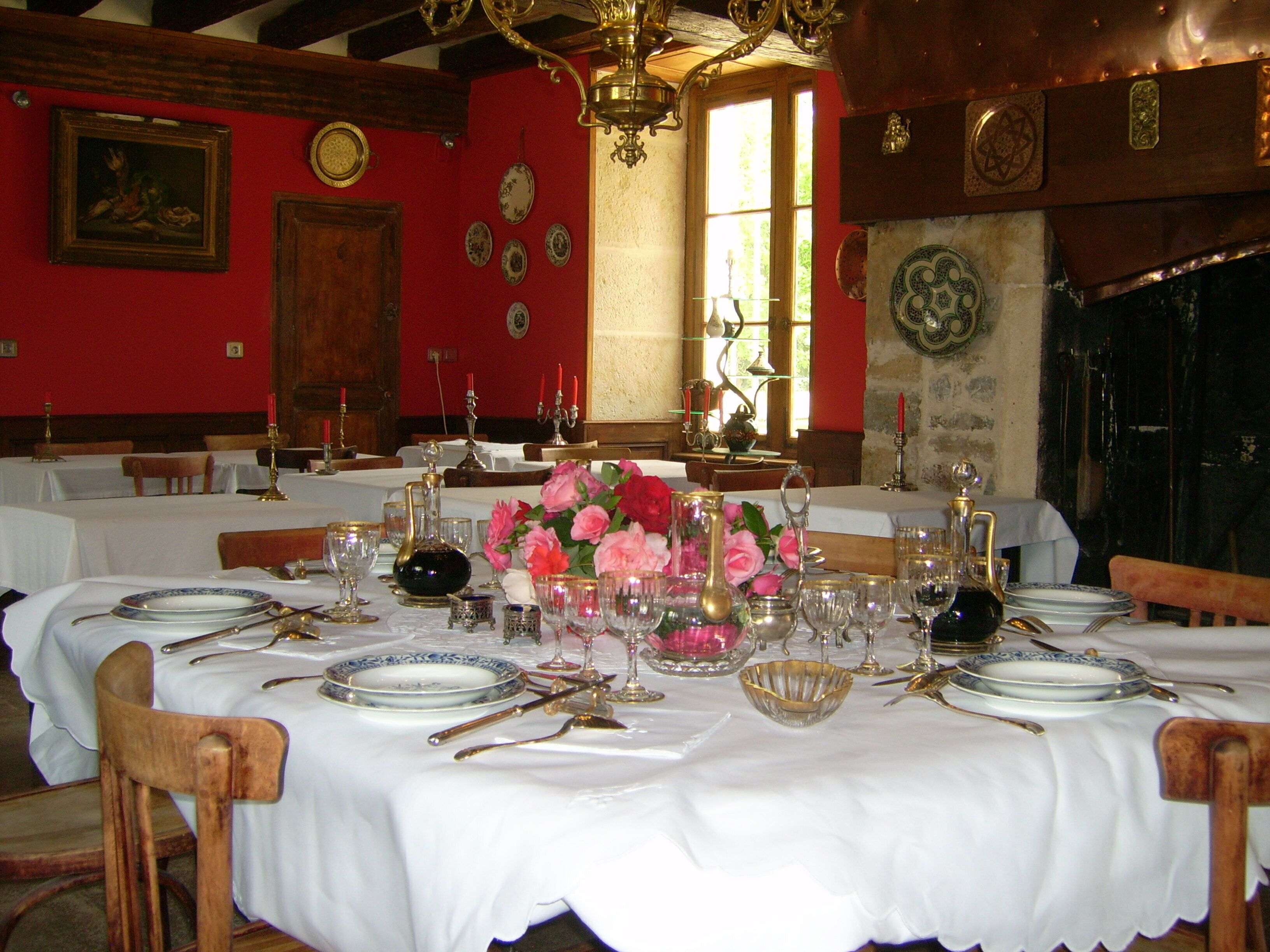 Een eetzaal met gedekte tafels voor een maaltijd, met witte tafellinnen, bestek en bloemstukken.