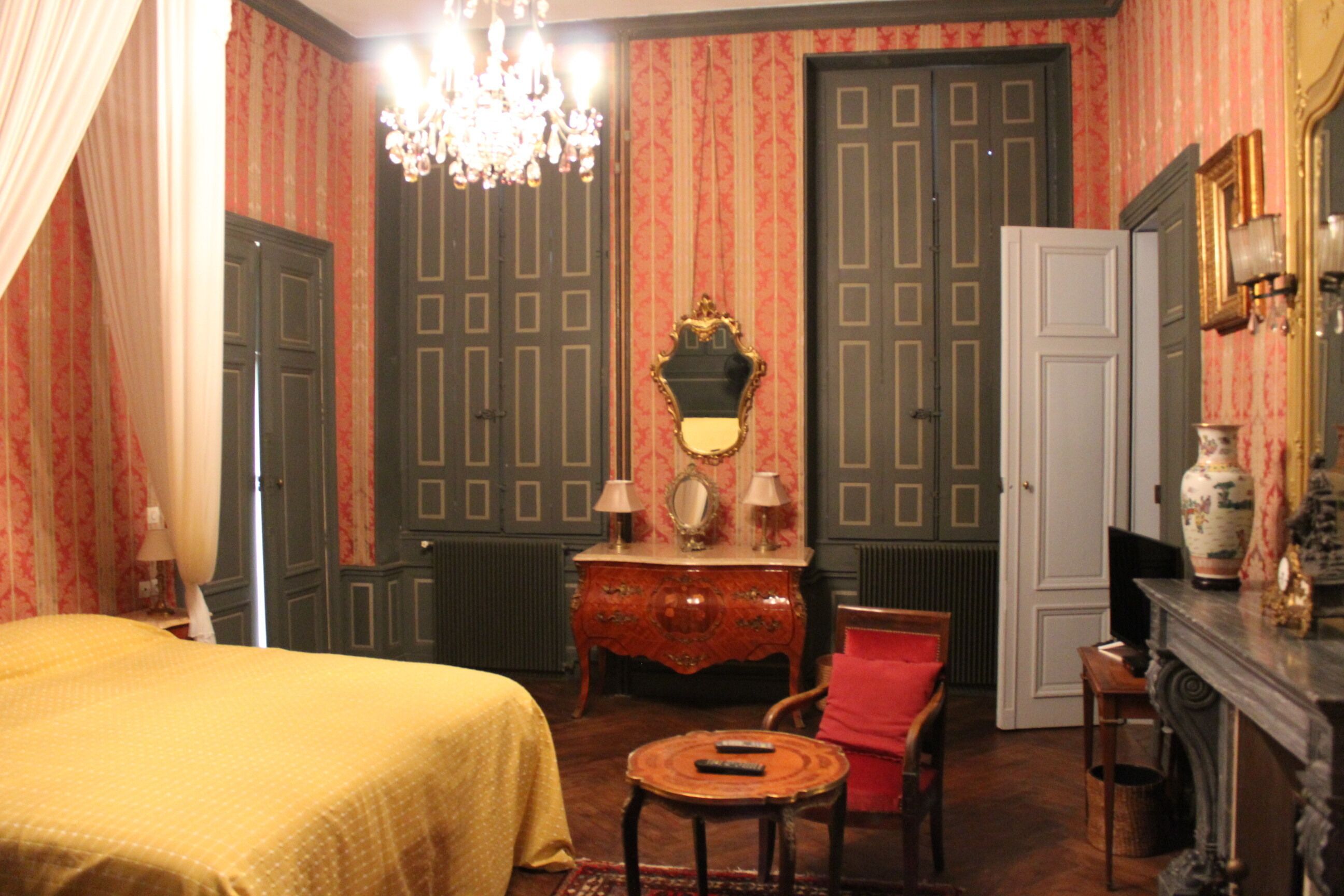 Una habitación con cama, cómoda, silla, mesa y espejo.