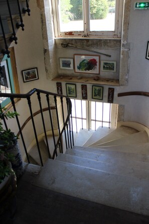 A staircase with a handrail, a window with a view of greenery outside, and several framed pictures on the wall. - Island Castle, Avallon, Vézelay (Island)