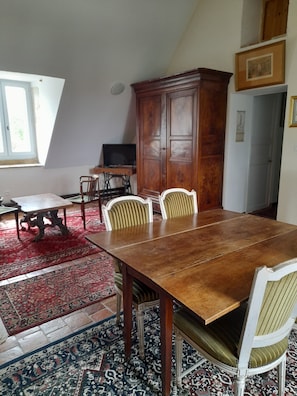 Zona pranzo con tavolo e sedie in legno, un tappeto rosso decorato e un grande armadio in legno.