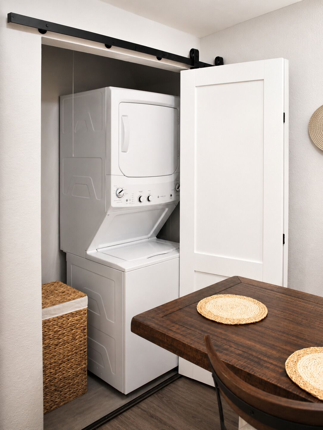 A laundry room with a front-loading washer and dryer, a wooden table with woven placemats, and a basket.