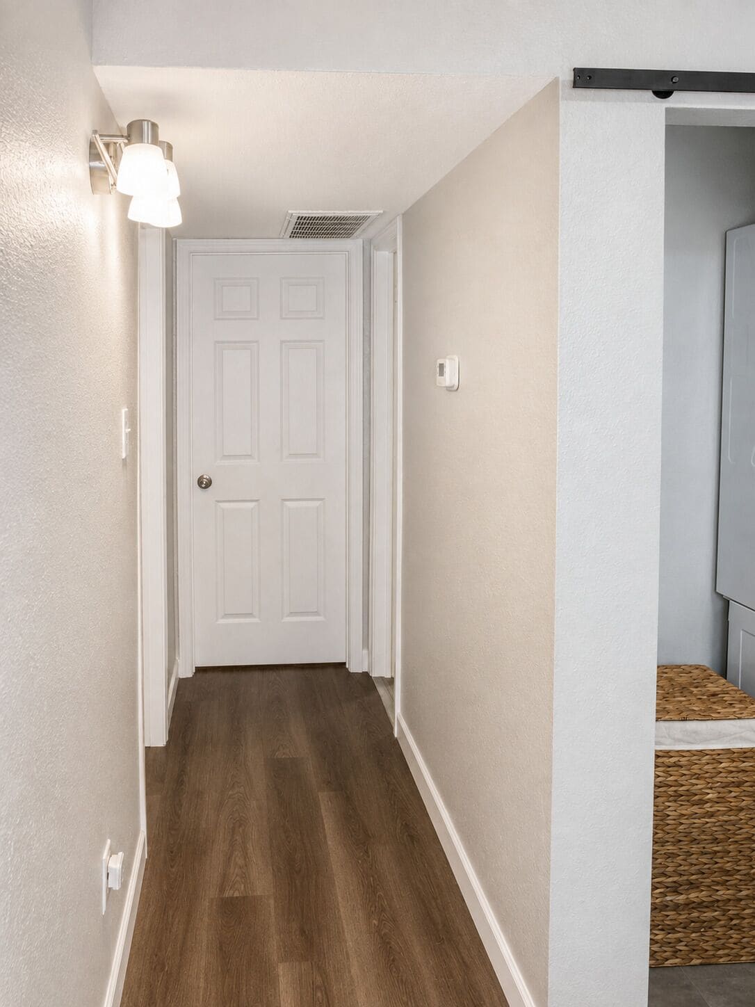 Un couloir avec une porte blanche, un interrupteur et un luminaire fixé au mur.