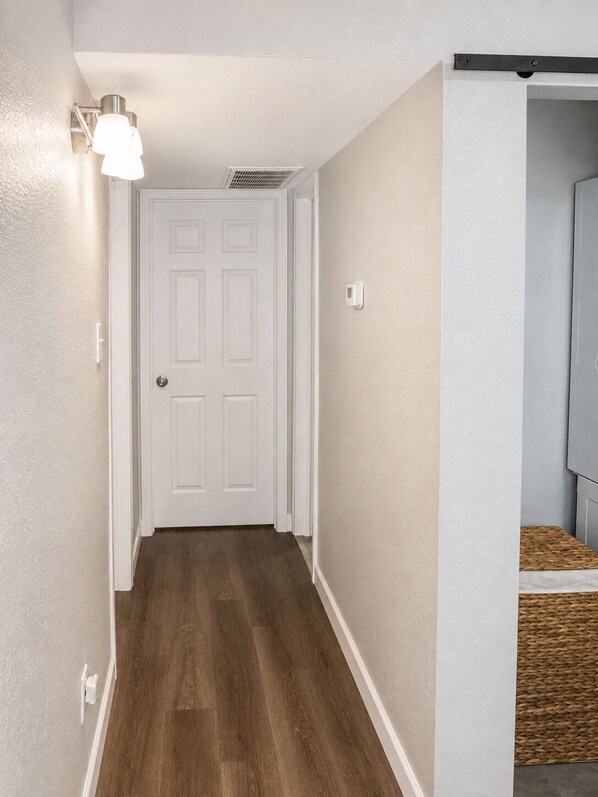 A hallway with a white door, light switch, and a wall-mounted light fixture.