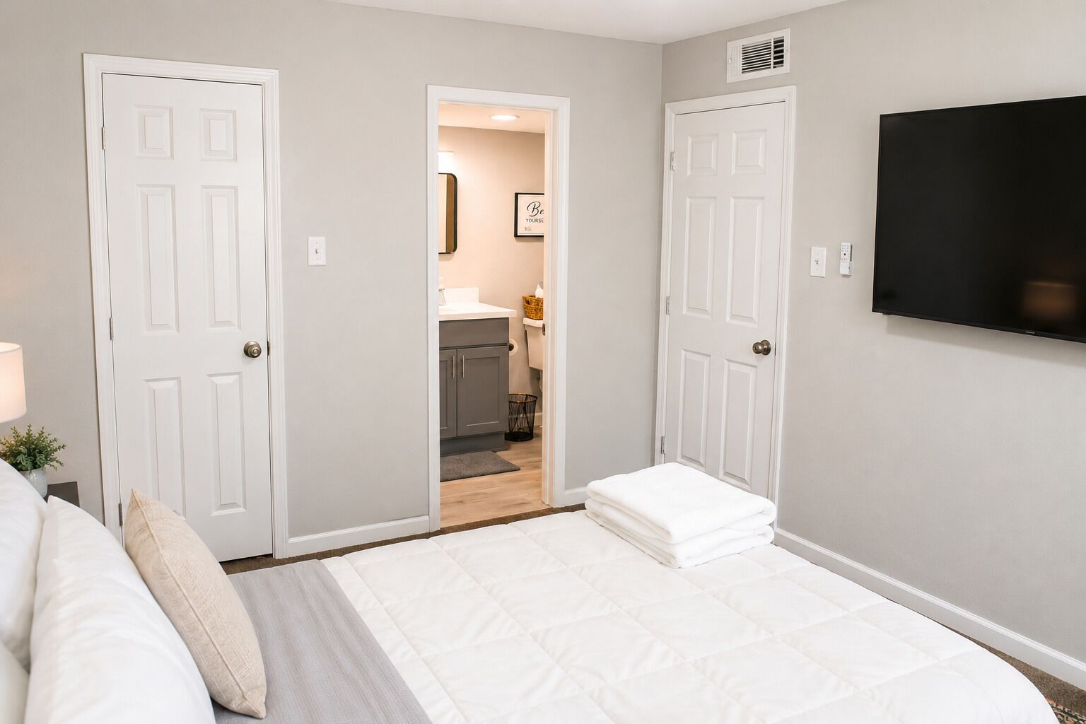 Une chambre à coucher avec un lit, un téléviseur fixé au mur et une porte donnant sur une salle de bain.