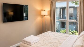 Habitación de hotel con cama, televisor de pantalla plana en la pared, lámpara de pie y ventana con cortinas.