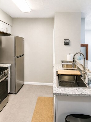 A modern kitchen with a stainless steel refrigerator, a built-in oven, a sink with a faucet, and a countertop with a cutting board.