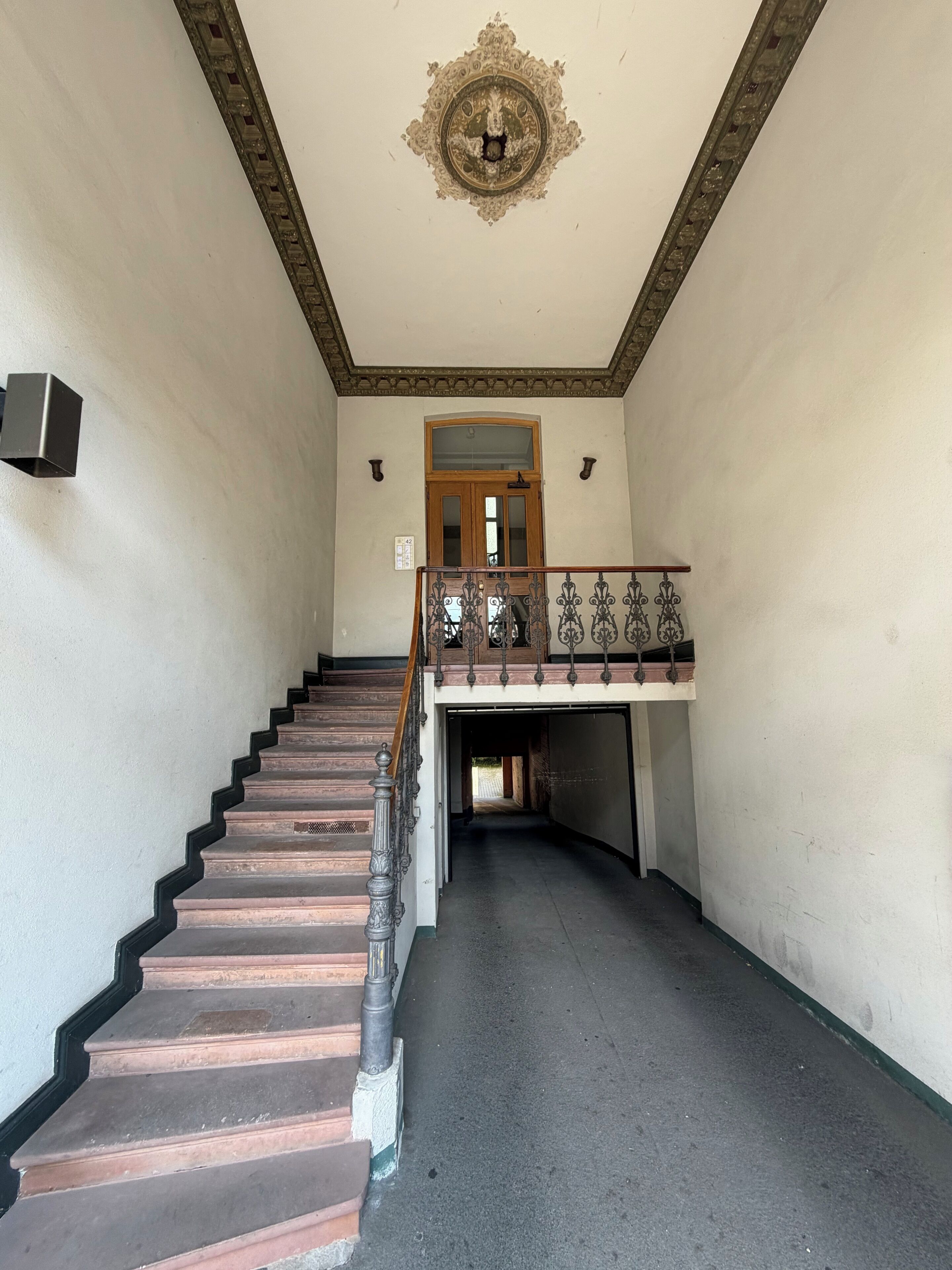 A staircase leading to a landing with a decorative ceiling and a wooden door.